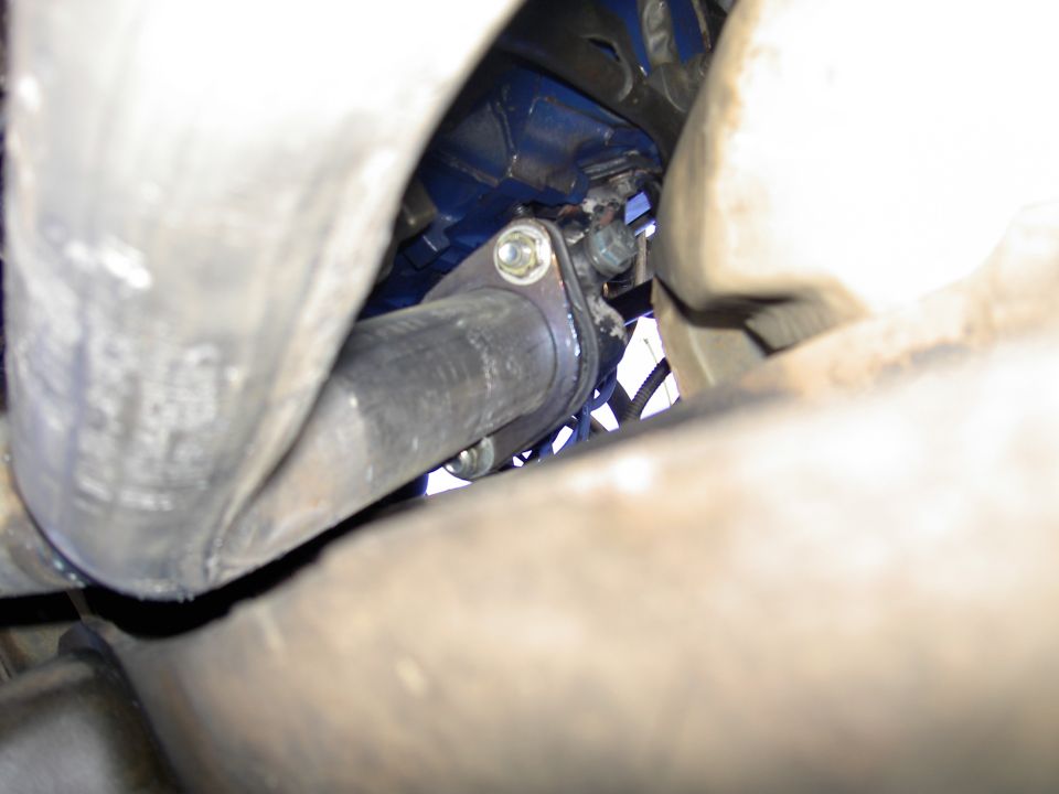 Underside close-up of a header flange bolted to a blue engine block beside a rusty exhaust pipe