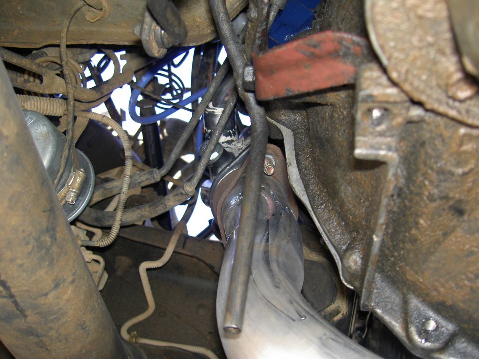 Underside view of a header collector and stainless downpipe routed past the frame rail of a 4x4