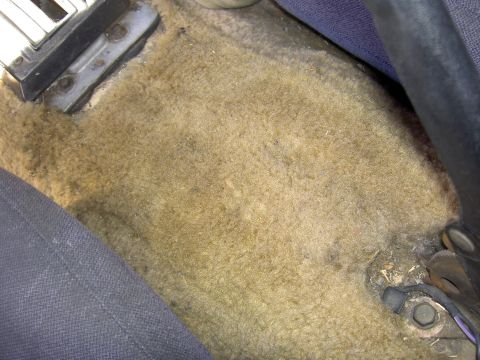 1982 Ford Mustang - Close-up view of the worn carpet and floor hardware inside a vehicle's cabin.