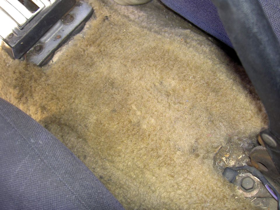Car floor carpet with some dirt and a bit of the driver's seat and center console visible