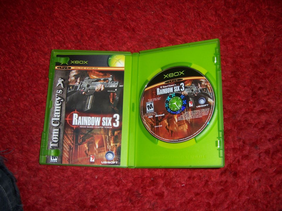 Open green Xbox game case with Tom Clancy's Rainbow Six 3 disc and cover art visible on a red carpet