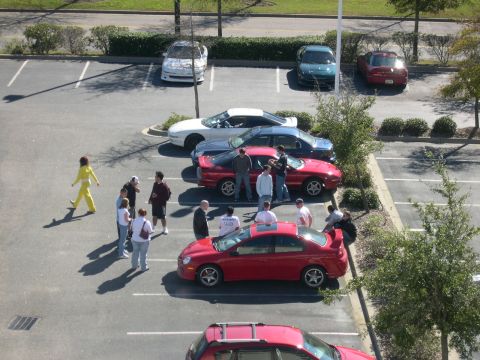 1997 Ford Probe - Several cars are parked in a lot, with a group of people gathered around a red sedan.