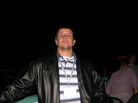 1997 Ford Probe - A man stands in front of a dark background, wearing a leather jacket over a striped shirt and a lanyard with a badge.
