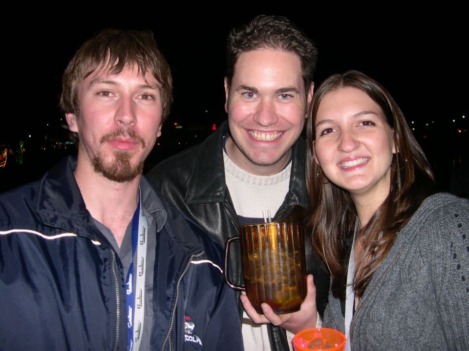 Three smiling people at an event, one holding a large amber mug