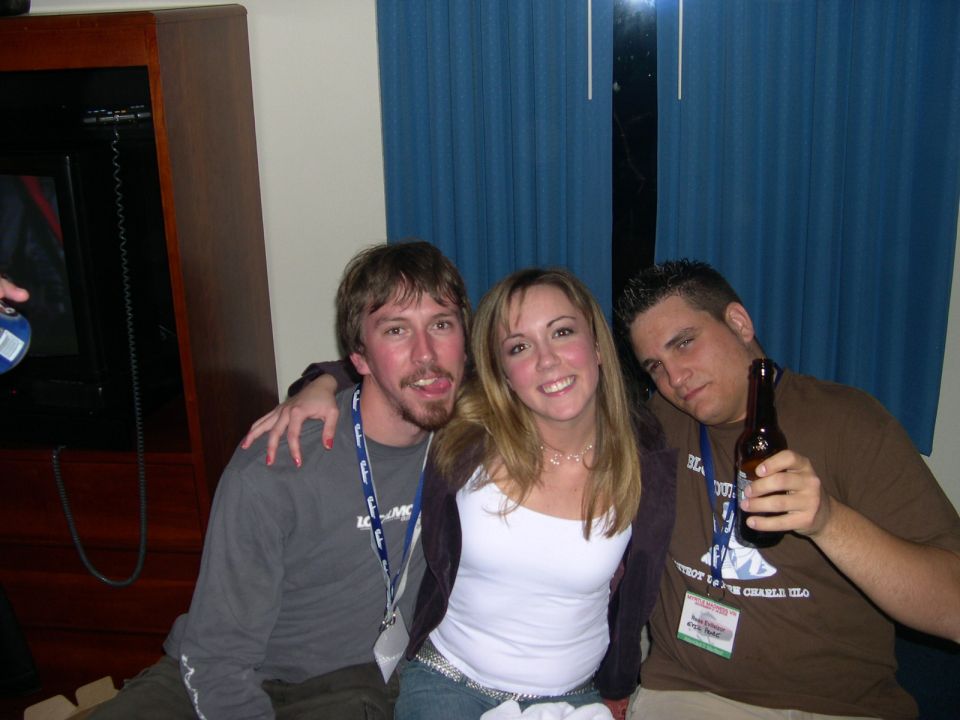 Three people are posing for a photo. The person on the left is sticking their tongue out. The person in the middle is smiling. The person on the right is holding a beer bottle