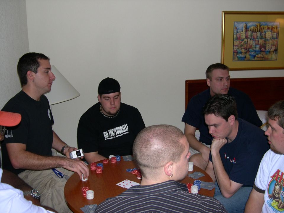 Poker game in progress with five men around a table, chips and cards visible