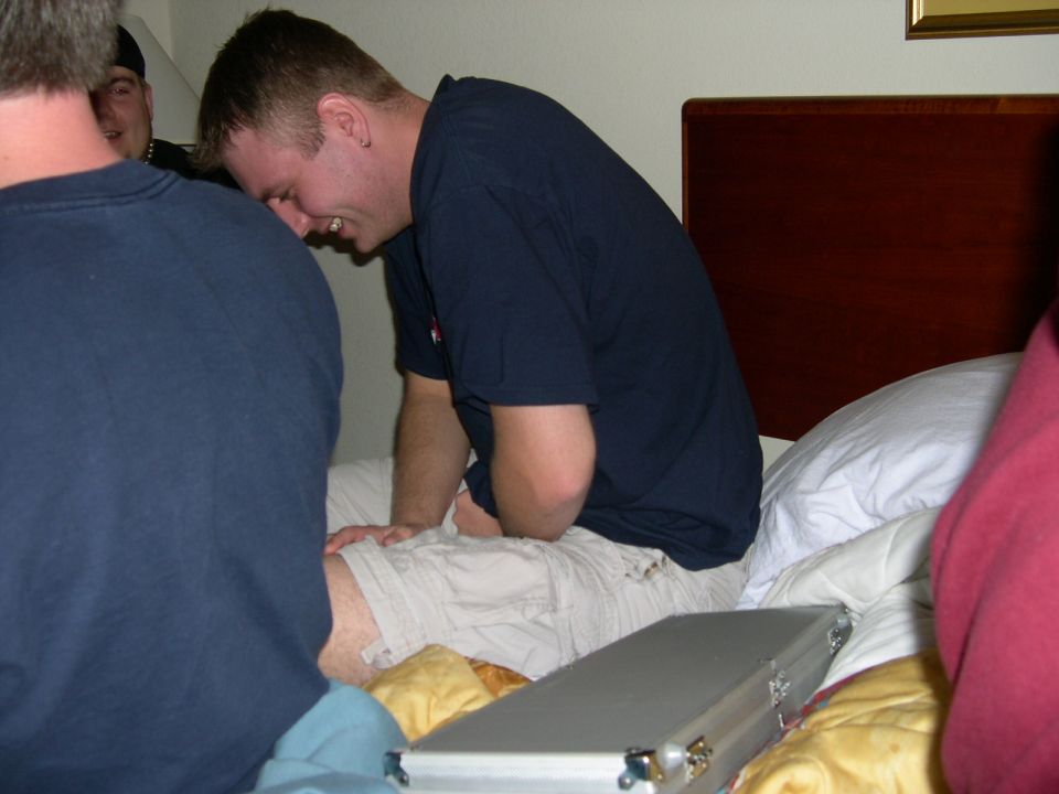 Three people on a bed, one man laughing with his head down