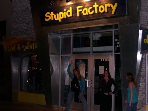 1997 Ford Probe - Three women stand outside a building with a prominent "Stupid Factory" sign.