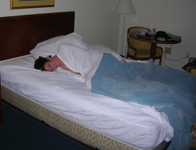 Person sleeping in a hotel bed under a blue blanket