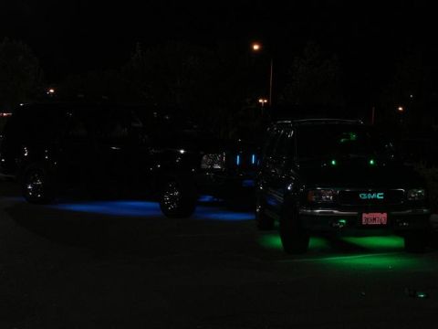 2000 Ford Excursion - Two SUVs are parked at night, each with different colored underglow lighting visible.