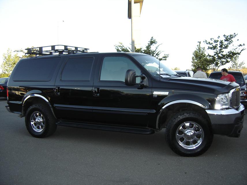 Black Ford Excursion SUV with roof rack and chrome wheels, 3/4 front side view in parking lot