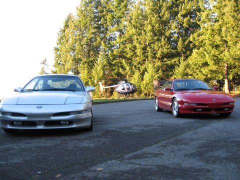 1994 Ford Probe - Two Ford Probes are parked side-by-side with a helicopter behind them.