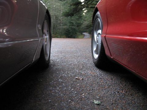 1994 Ford Probe - Two cars are parked on a gravel road, with a narrow paved road visible in the distance between trees.