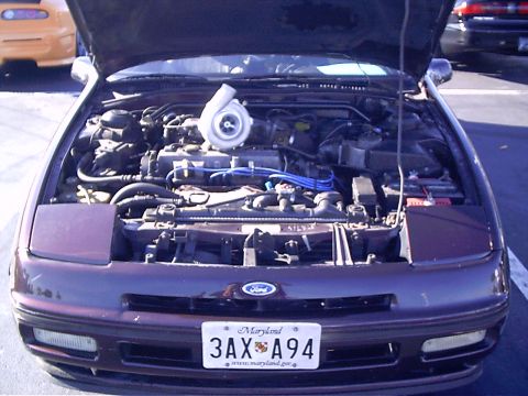 1995 Ford Probe - Engine bay of a 1995 Ford Probe, modified with a turbocharger. Another car is visible in the background.