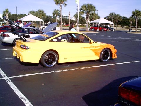 1995 Ford Probe - A yellow sports car with a custom paint job and a large spoiler is parked at an outdoor event.