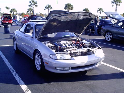 1995 Ford Probe - A silver Mazda MX-6 is parked with its hood open, revealing the engine compartment, at an outdoor car gathering.