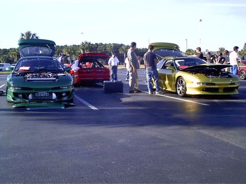 1995 Ford Probe - A gold sports car is parked with its hood open, alongside other vehicles at an outdoor gathering.