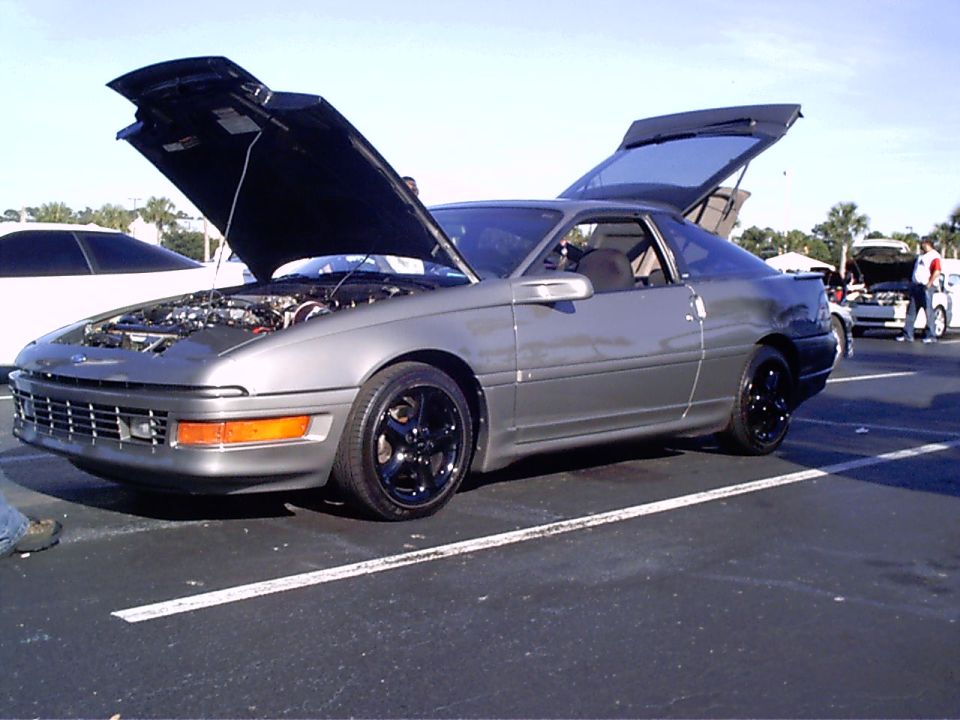 Gray 1995 Ford Probe with hood and trunk open, parked at an outdoor event. Another car is visible to the left