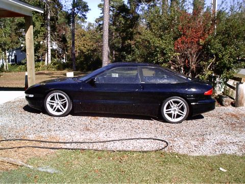 1995 Ford Probe - A black 1995 Ford Probe is parked on a gravel driveway next to a house and trees.