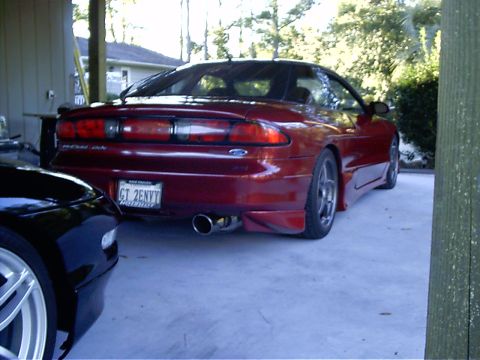 1995 Ford Probe - A red Ford Probe is parked in a driveway, partially obscured by another vehicle.