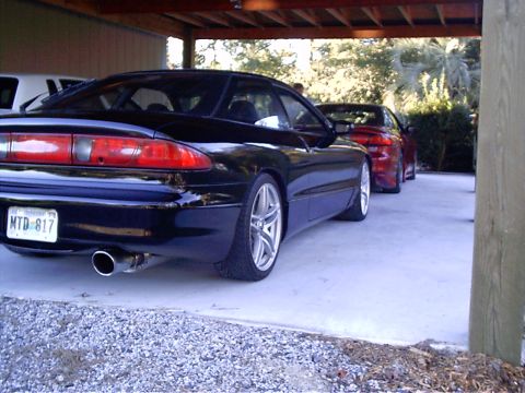 1995 Ford Probe - Two coupes, a black 1995 Ford Probe and a red car, are parked under a carport.
