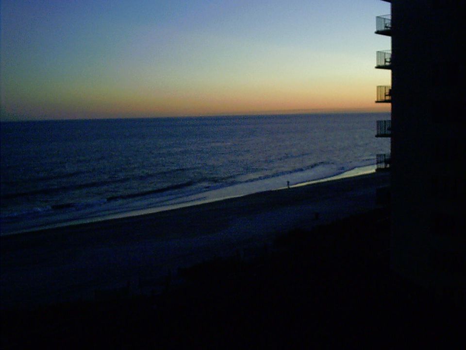 Dark beach scene with ocean waves and a building with balconies at dusk