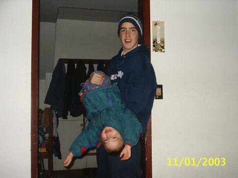 1989 Ford Bronco - A young man holds a baby upside down in a doorway, with coats hanging in the background.