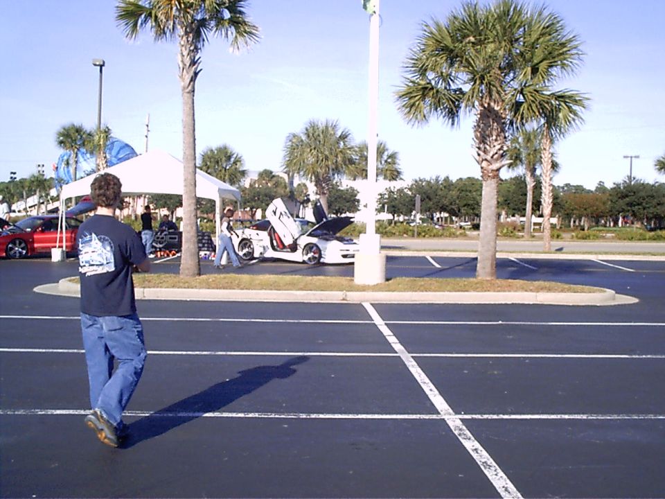 White sports car with butterfly doors open, hood up, parked in a lot