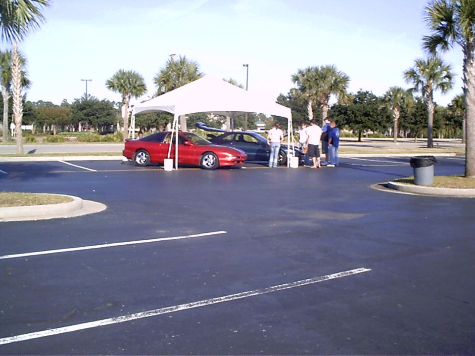 Red 1995 Ford Probe and a dark sedan parked under a white canopy at an outdoor event