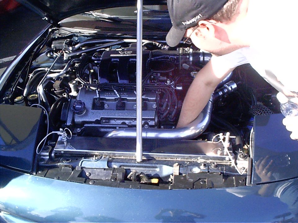 Person working on engine bay, hood open. Aftermarket intake pipe visible