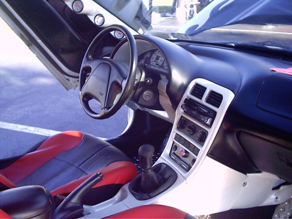 Car interior shows red and black seats, aftermarket stereo, and gauges on the door panel