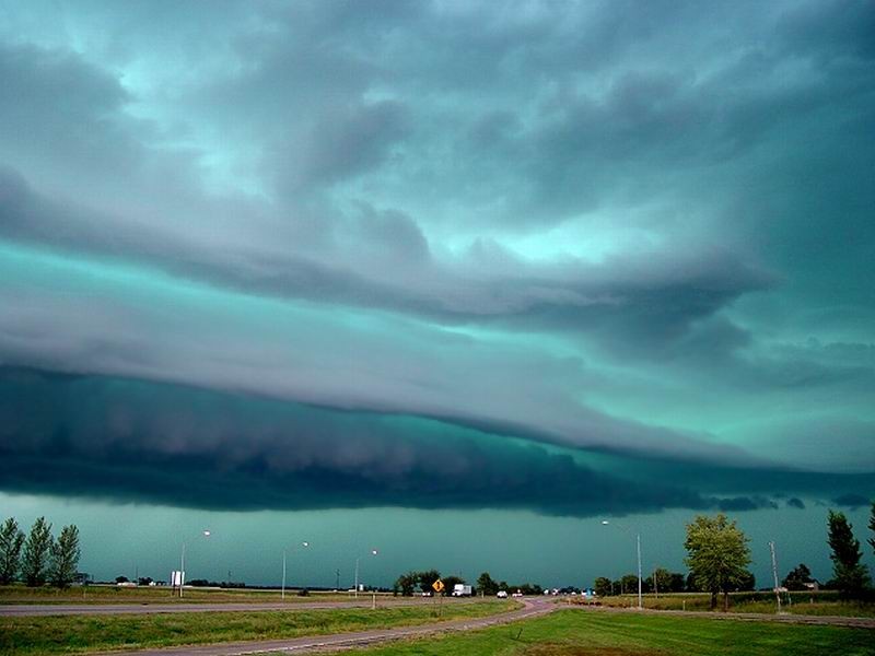 Green shelf-cloud storm rolling over a flat highway landscape at dusk