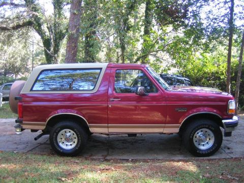 1994 Ford Bronco - Side profile of a red 1994 Ford Bronco with a tan removable top and spare tire.