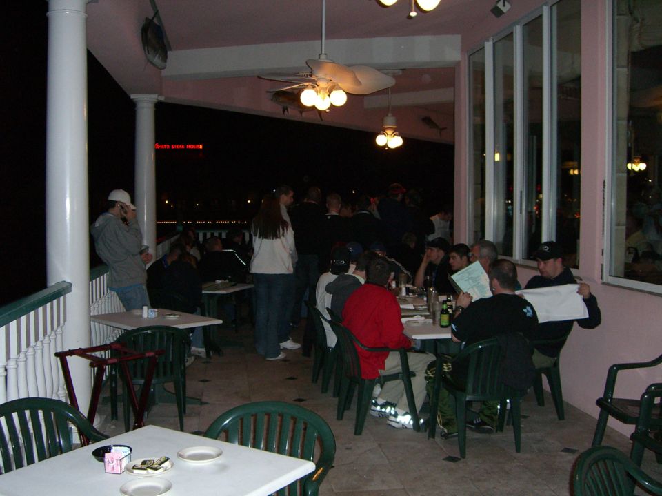People sit at tables on a covered patio at night, some looking at menus