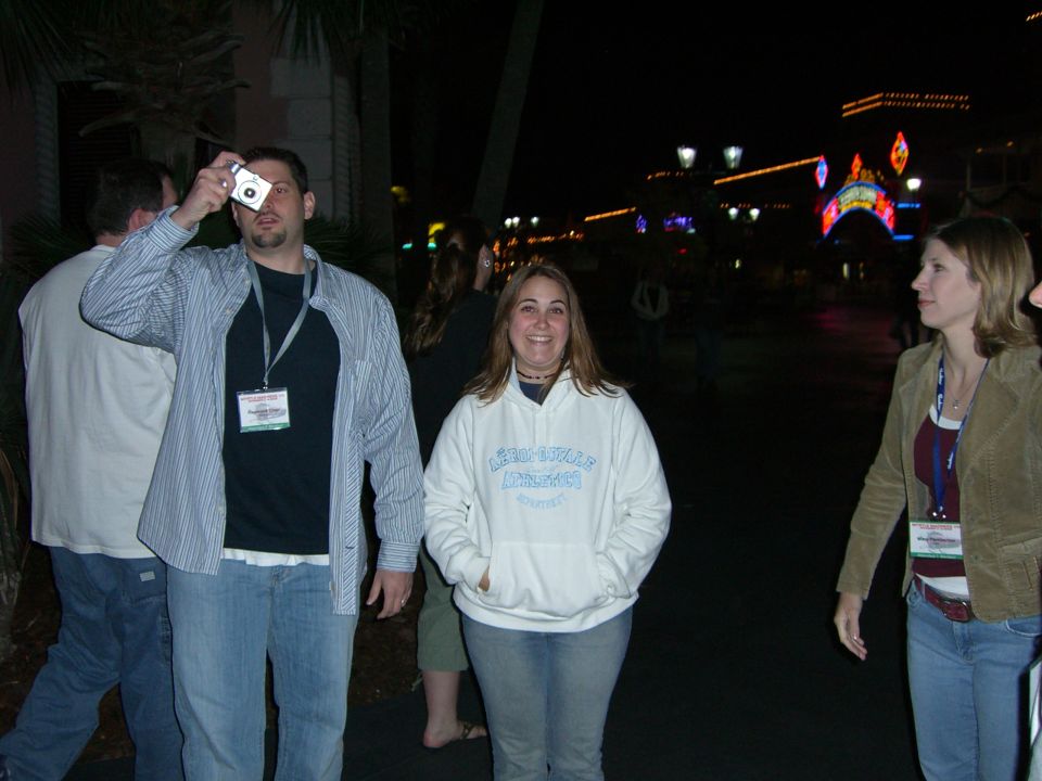 People standing outside at night with colorful illuminated buildings in the background