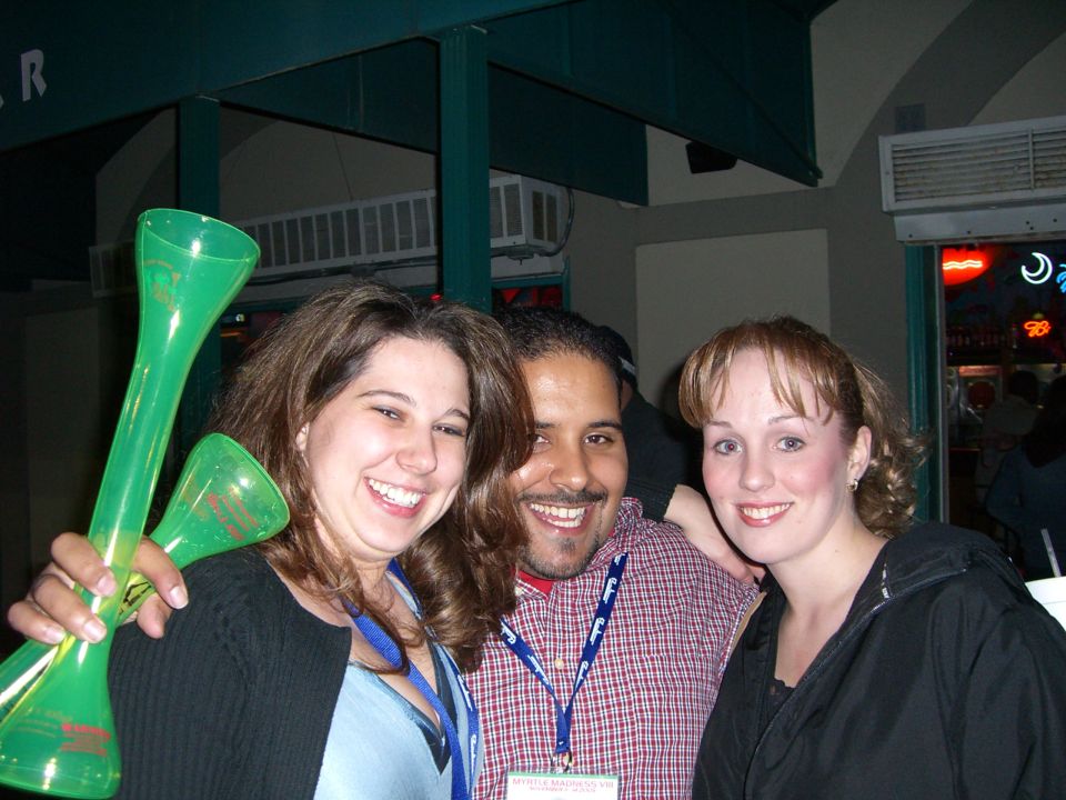Three people smiling, one holding green novelty horns
