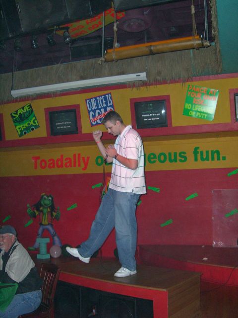 1996 Ford Probe - A man performs on stage in a themed entertainment venue with frog imagery and humorous signs.