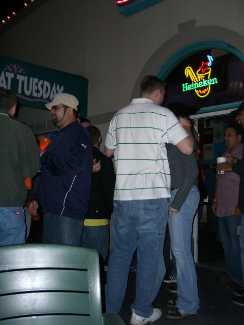 1996 Ford Probe - A group of people are seen socializing in a dimly lit establishment, with a neon Heineken sign visible in the background.