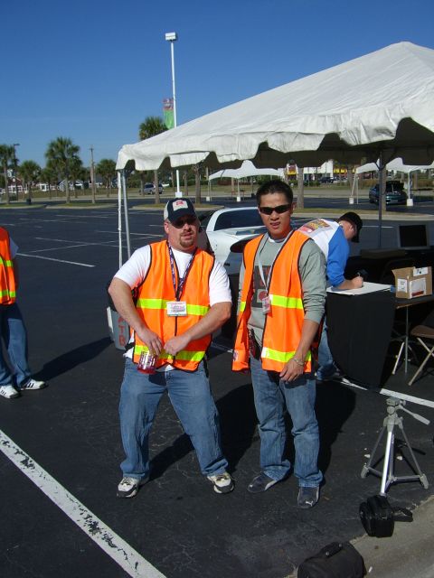 1996 Ford Probe - Two men in orange safety vests stand in a parking lot under a white tent, with a white car visible in the background.
