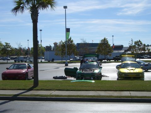 1996 Ford Probe - Several sports cars are parked in a lot on a sunny day, with one undergoing maintenance.