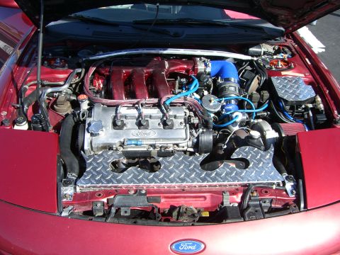 1996 Ford Probe - The engine bay of a red 1996 Ford Probe shows a V6 engine with custom modifications and diamond plate accents.