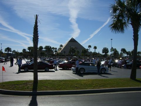 1996 Ford Probe - A white sports car is parked in a lot filled with other vehicles, with a large pyramid structure visible in the distance under a blue sky.