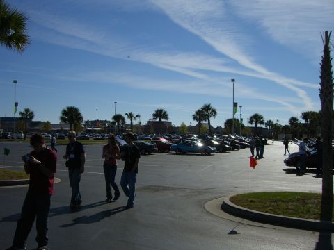 1996 Ford Probe - A gathering of vehicles and people in a large outdoor parking area on a sunny day.