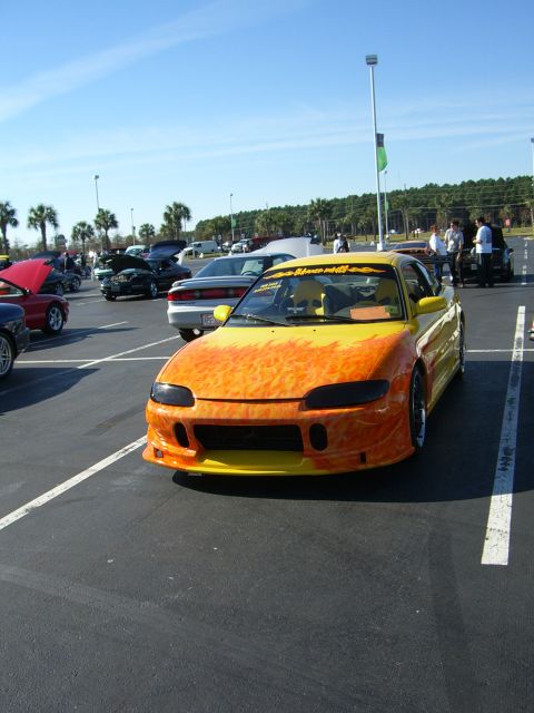 1996 Ford Probe - A customized sports car with a flame paint job is parked in a lot during a car show.