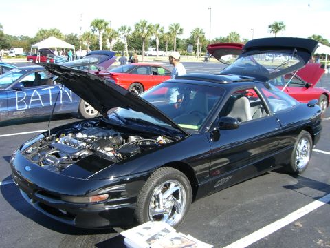 1996 Ford Probe - A black 1996 Ford Probe GT is displayed with its hood and trunk open at a car show, with other vehicles in the background.