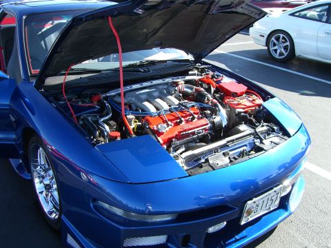 1996 Ford Probe - Engine bay of a blue 1996 Ford Probe, with the hood fully open. A white car is visible in the background.