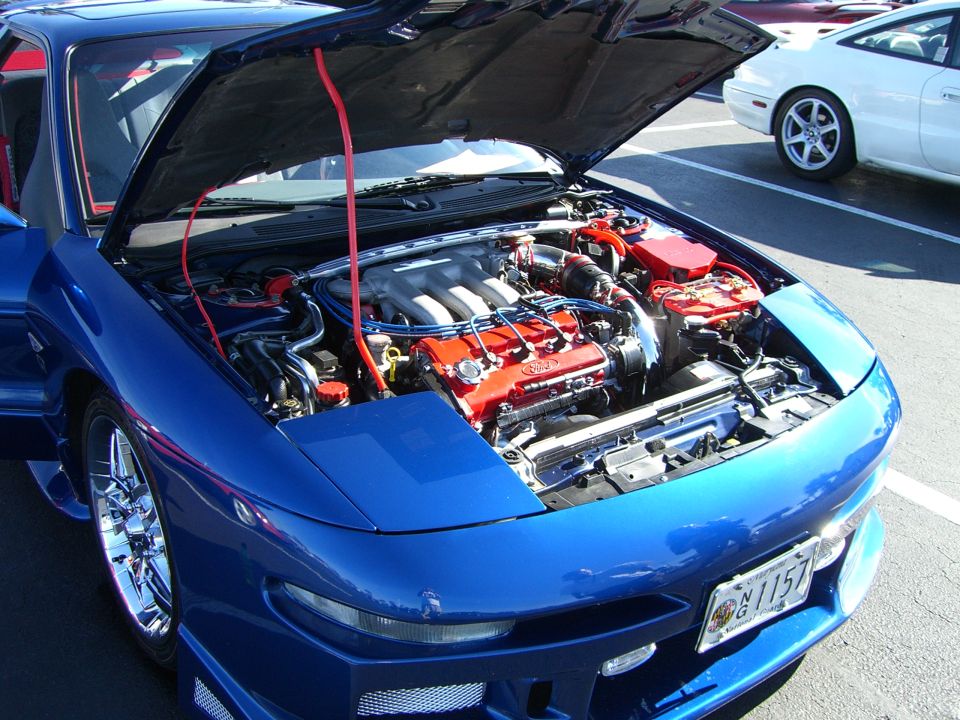 Blue 1996 Ford Probe with hood open, showing the V6 engine. Another white car is parked nearby