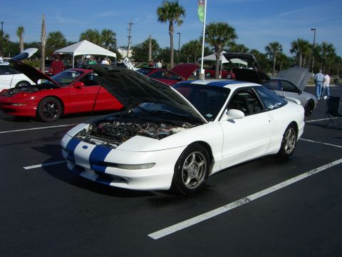 1996 Ford Probe - A white Ford Probe with blue racing stripes is displayed with its hood open at a car show.