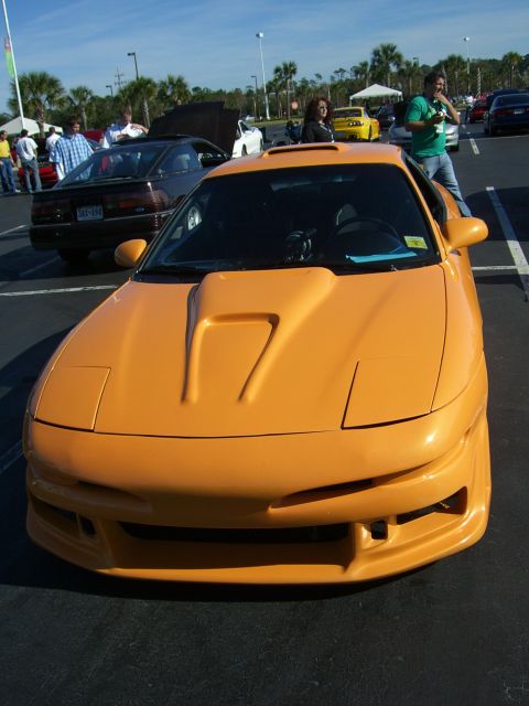 1996 Ford Probe - A bright orange sports coupe with a distinctive hood scoop is the focus of this photo, with other vehicles and people in the background.