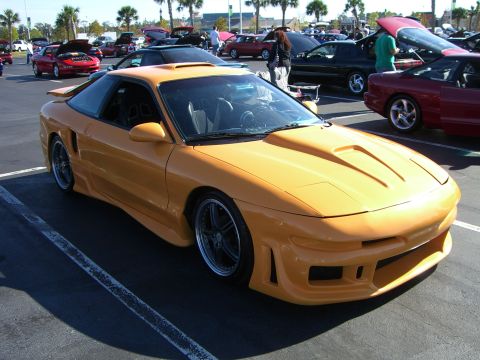 1996 Ford Probe - A modified yellow sports car is parked in a lot with other vehicles.